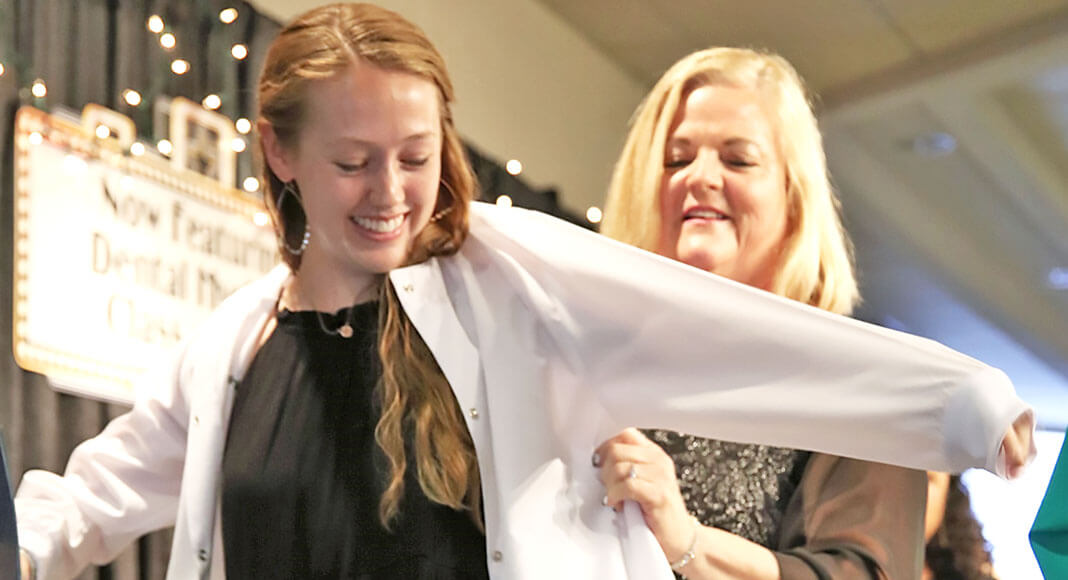 TSTC Dental Hygiene instructor Lucretia Human places a lab coat on Carrie Portwood, a graduating TSTC Dental Hygiene student, to recognize her as a dental hygienist during a recent pinning ceremony. (TSTC photo.)